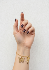 Mano femenina con pulsera dijes mariposas contra pared blanca minimalista | Gheller