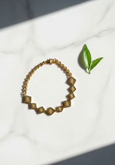 Pulsera dijes rombo dorada flat lay sobre mármol minimalista | Gheller