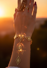 Brazo femenino con pulsera dijes rombo dorados al atardecer reflejos | Gheller