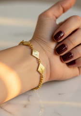 Close-up pulsera dijes rombo dorados en muñeca femenina sobre mármol | Gheller