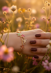 Mano femenina con pulsera dijes mariposas entre flores silvestres golden hour | Gheller
