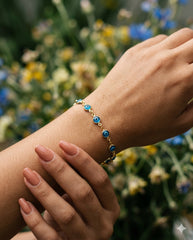 Close-up pulsera ojo turco dorada en muñeca con flores silvestres | Gheller