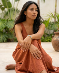 Modelo sentada con pulsera ojo turco, vestido terracota entre plantas | Gheller
