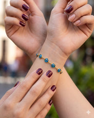 Muñecas cruzadas con pulsera ojo turco, uñas color vino | Gheller Joyería