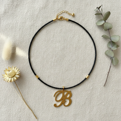 Dije inicial B en oro laminado 18k — composición flatlay con accesorios