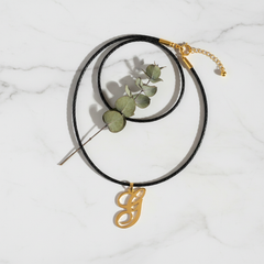 Dije inicial G en oro laminado 18k — composición flatlay con accesorios