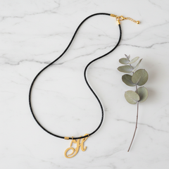 Dije inicial H en oro laminado 18k — composición flatlay con accesorios