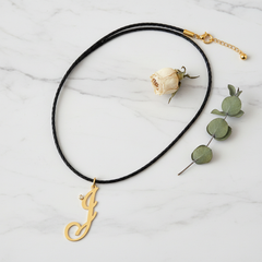 Dije inicial J en oro laminado 18k — composición flatlay con accesorios