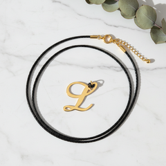 Dije inicial L en oro laminado 18k — composición flatlay con accesorios