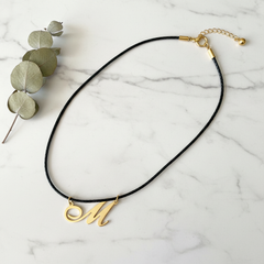 Dije inicial M en oro laminado 18k — composición flatlay con accesorios