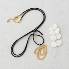 Dije inicial O en oro laminado 18k — composición flatlay con accesorios