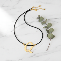 Dije inicial Q en oro laminado 18k — composición flatlay con accesorios