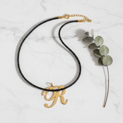 Dije inicial R en oro laminado 18k — composición flatlay con accesorios