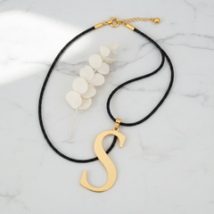 Dije inicial S en oro laminado 18k — composición flatlay con accesorios