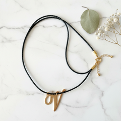 Dije inicial V en oro laminado 18k — composición flatlay con accesorios